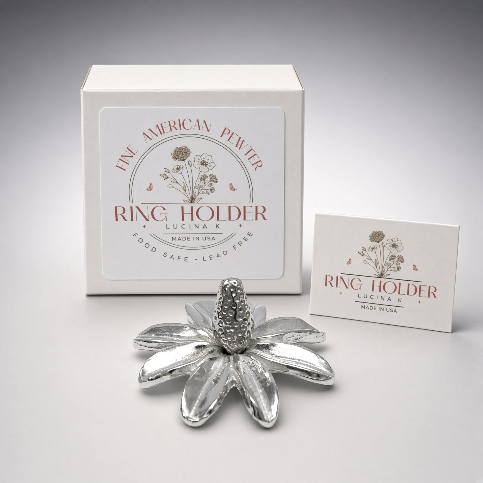 Pewter daisy ring holder in front of its white Fine American Pewter Ring Holder gift box and card