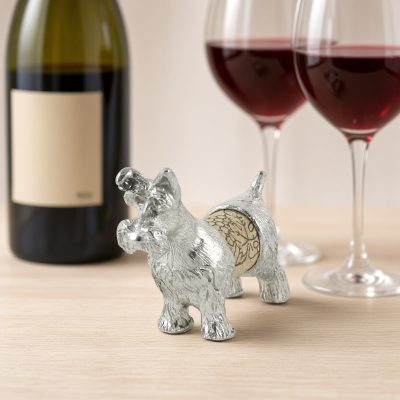 Lucina K Schnauzer Cork Pet, a solid pewter Schnauzer with a bearded muzzle and upright tail holding a wine cork, beside a wine bottle and two glasses of red wine