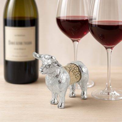 Lucina K Bull Cork Pet, a solid pewter horned bull holding a wine cork, beside a wine bottle and two glasses of red wine
