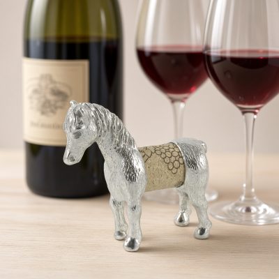 Lucina K Horse Cork Pet, a solid pewter standing horse with a flowing mane holding a wine cork, beside a wine bottle and two glasses of red wine