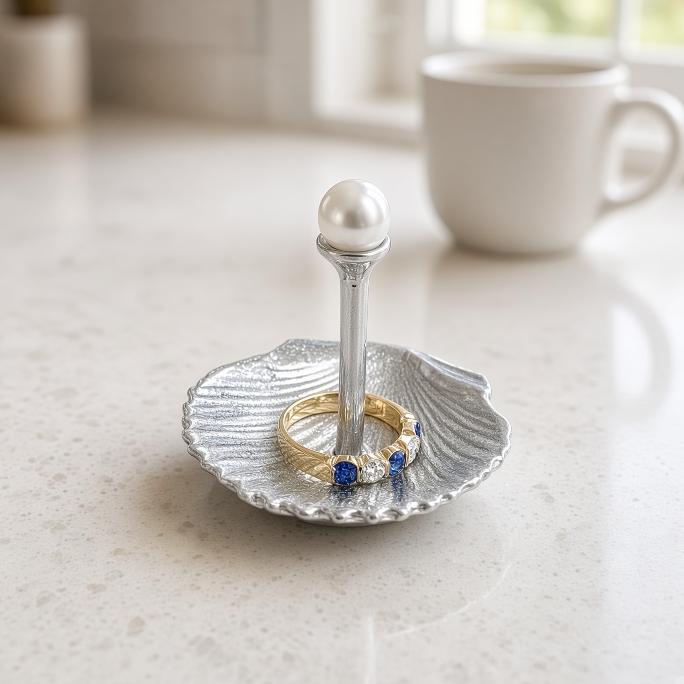Pewter pearl and shell ring holder with a gold ring over the post, on a white counter beside a mug, ring not included