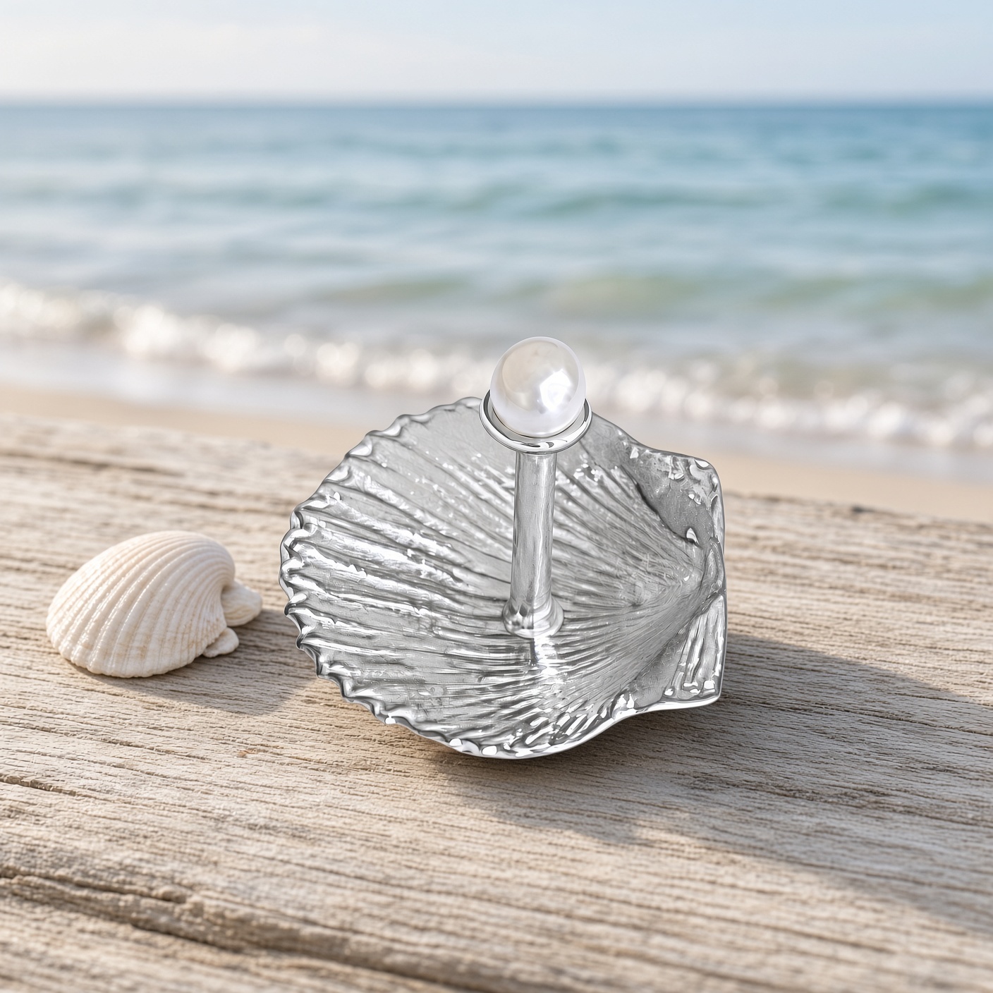 Pewter pearl and shell ring holder on driftwood at the beach beside a seashell