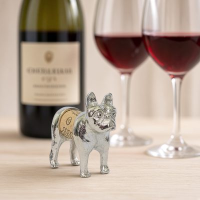 Lucina K Frenchie Cork Pet, a solid pewter French Bulldog with tall bat ears holding a wine cork, beside a wine bottle and two glasses of red wine