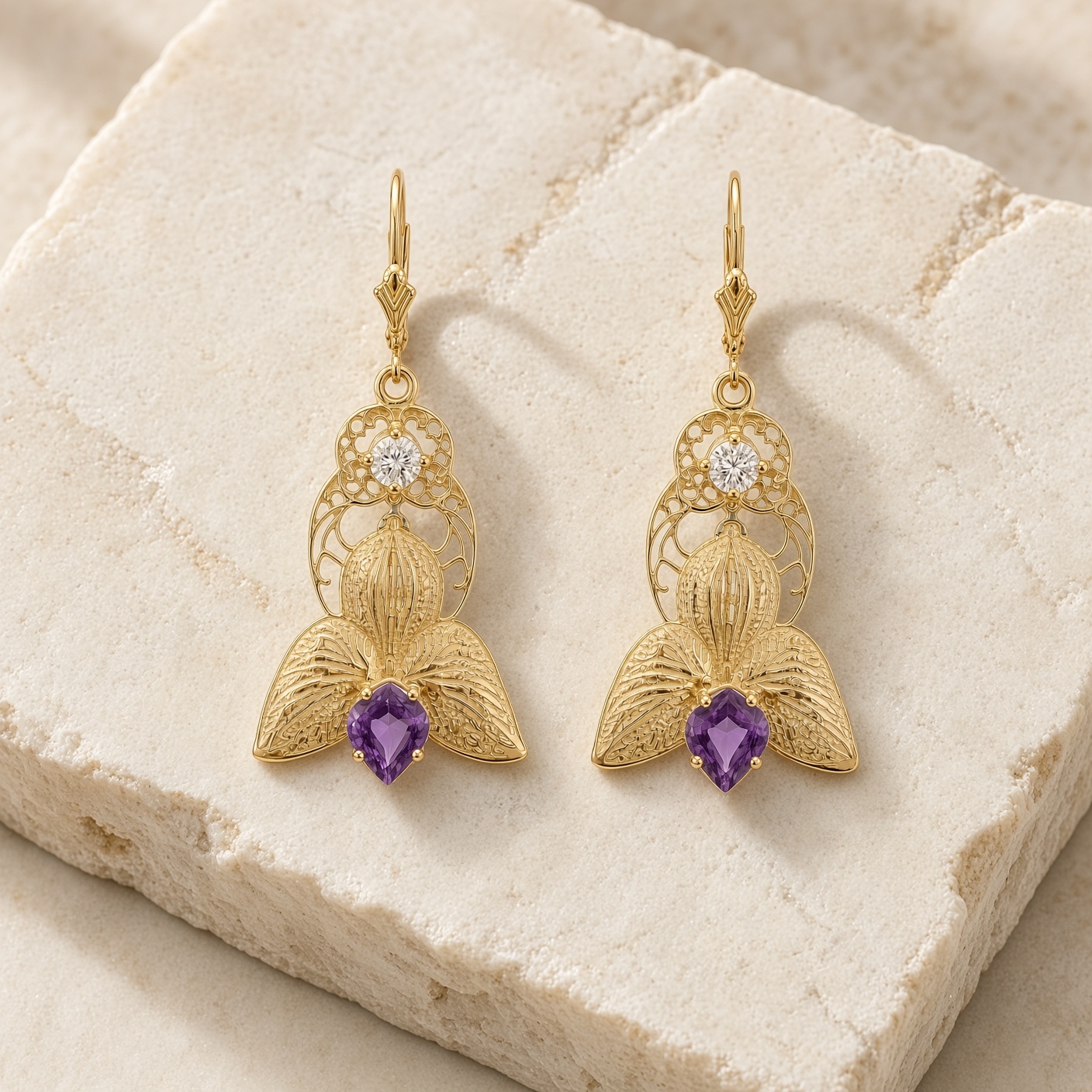 Orchid drop earrings in 14K gold with purple amethysts on a rough cream stone slab