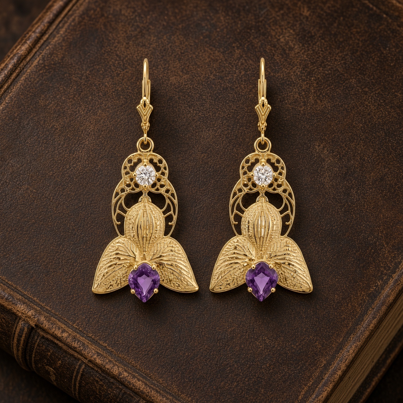 Gold orchid earrings with amethyst petal tips and diamond centers on a dark brown leather book