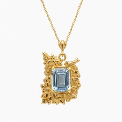 14K yellow gold pendant with an emerald-cut sky blue topaz framed by sculpted flowers and a small bird, on a gold chain, white background
