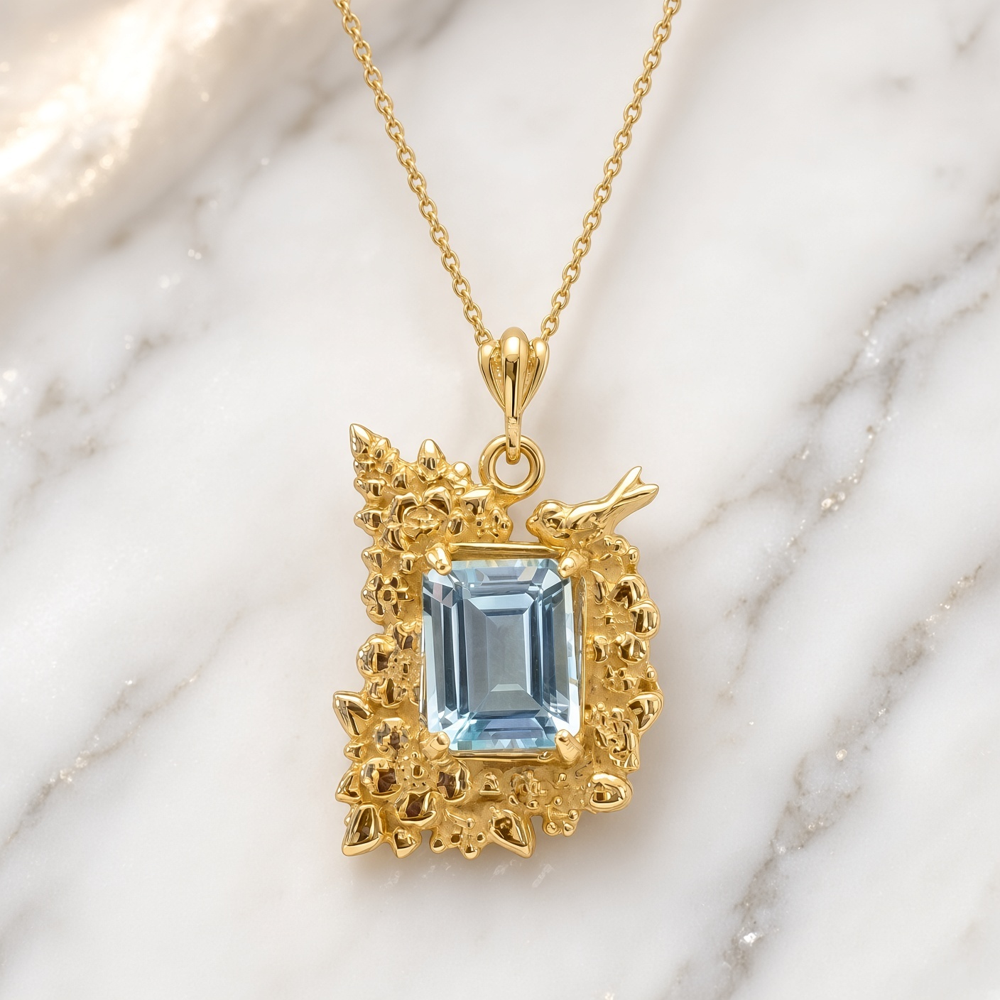 Emerald-cut sky blue topaz in a 14K gold flower and bird frame on white and gray marble