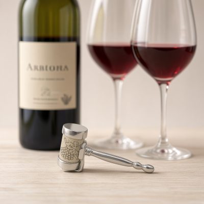 Lucina K Gavel Cork Pet, a pewter judge's gavel holding a wine cork, beside a wine bottle and two glasses of red wine