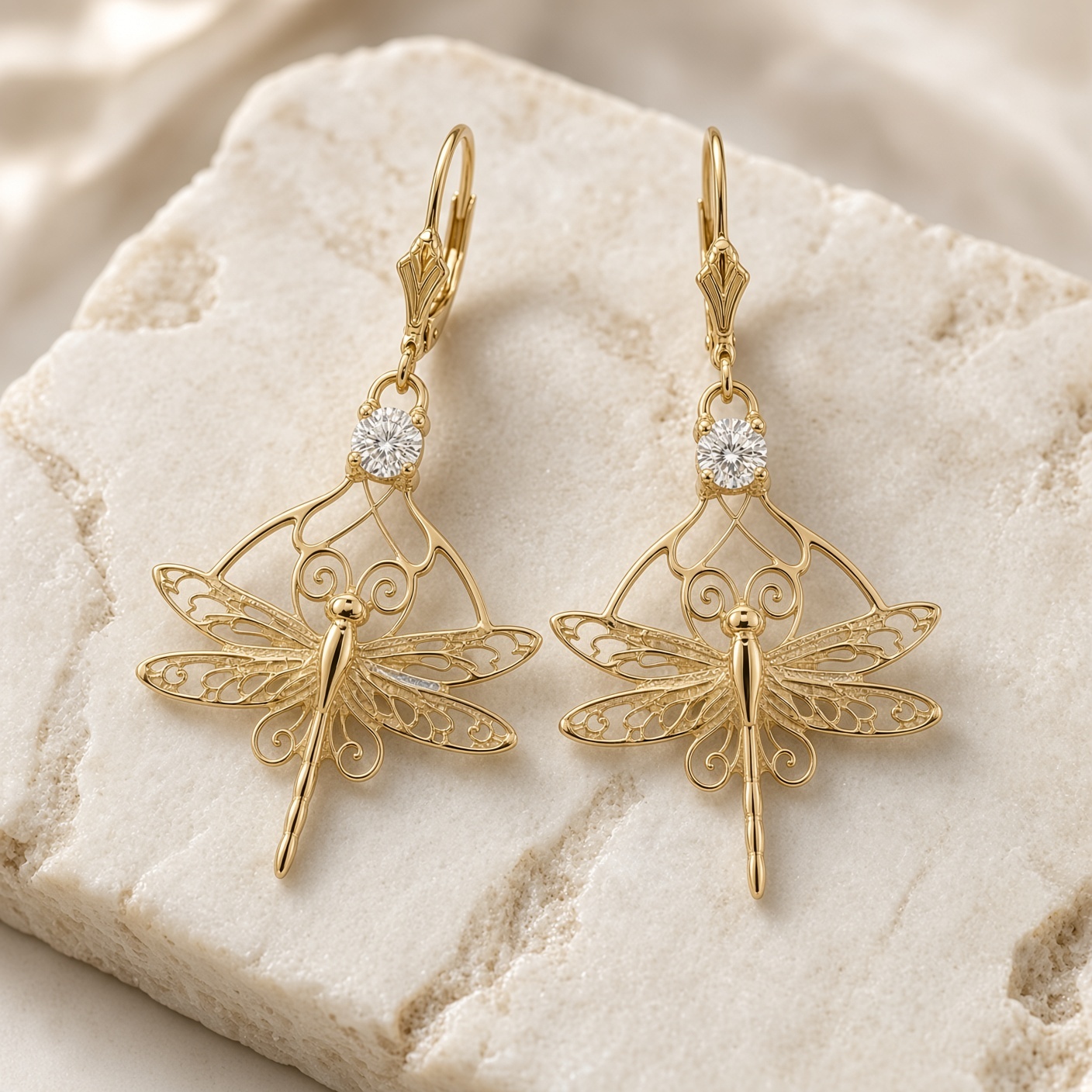 14K yellow gold dragonfly diamond earrings resting on a pale stone slab over cream linen
